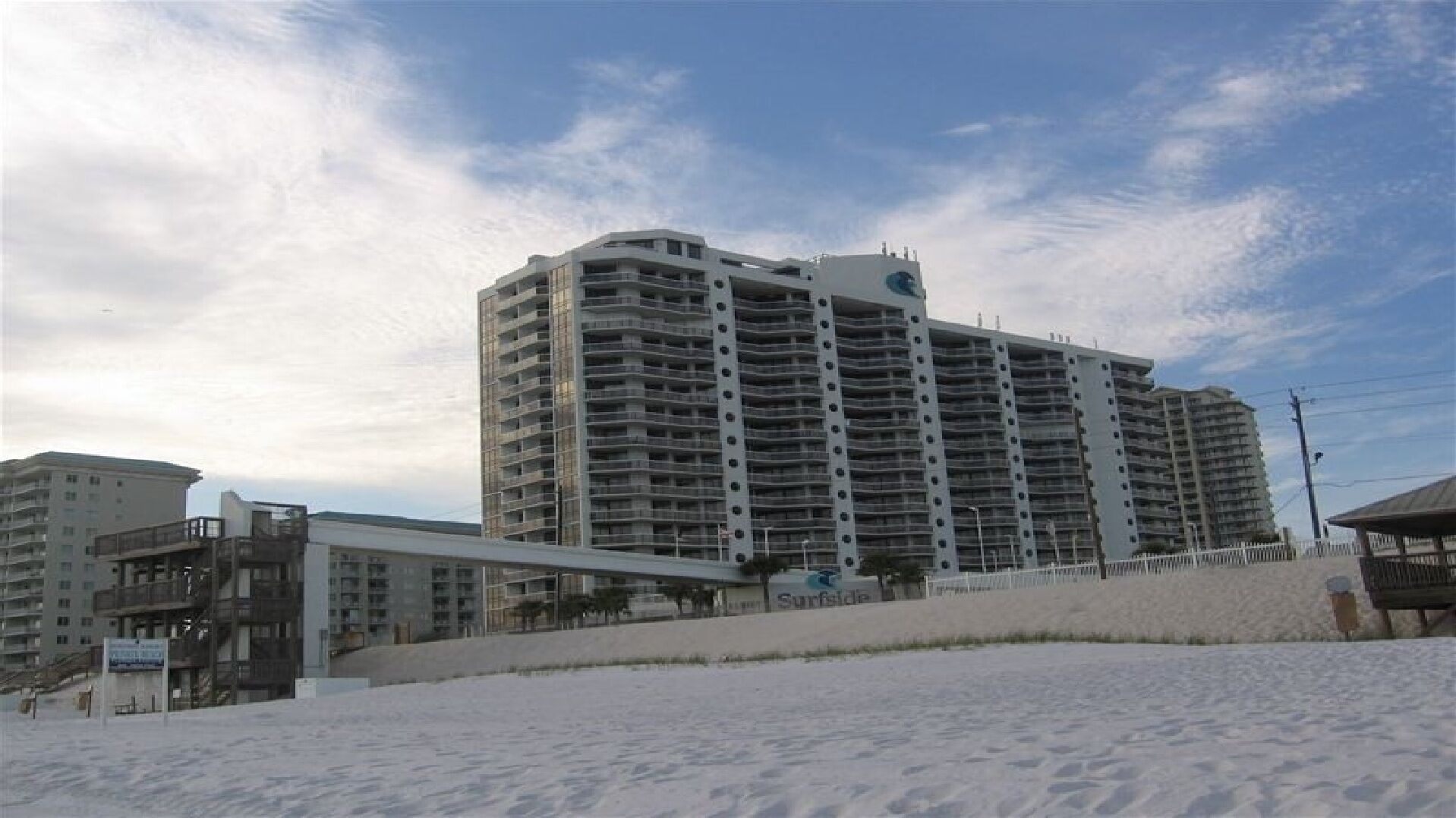 A high-rise hotel with multiple balconies, located near a beach.