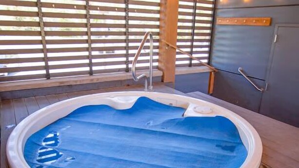 Un jacuzzi rond avec un escalier en métal, entouré d’une terrasse en bois et d’une rambarde en métal.