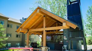 Un espace extérieur abrité avec des tables de pique-nique, des bancs en pierre et un barbecue.
