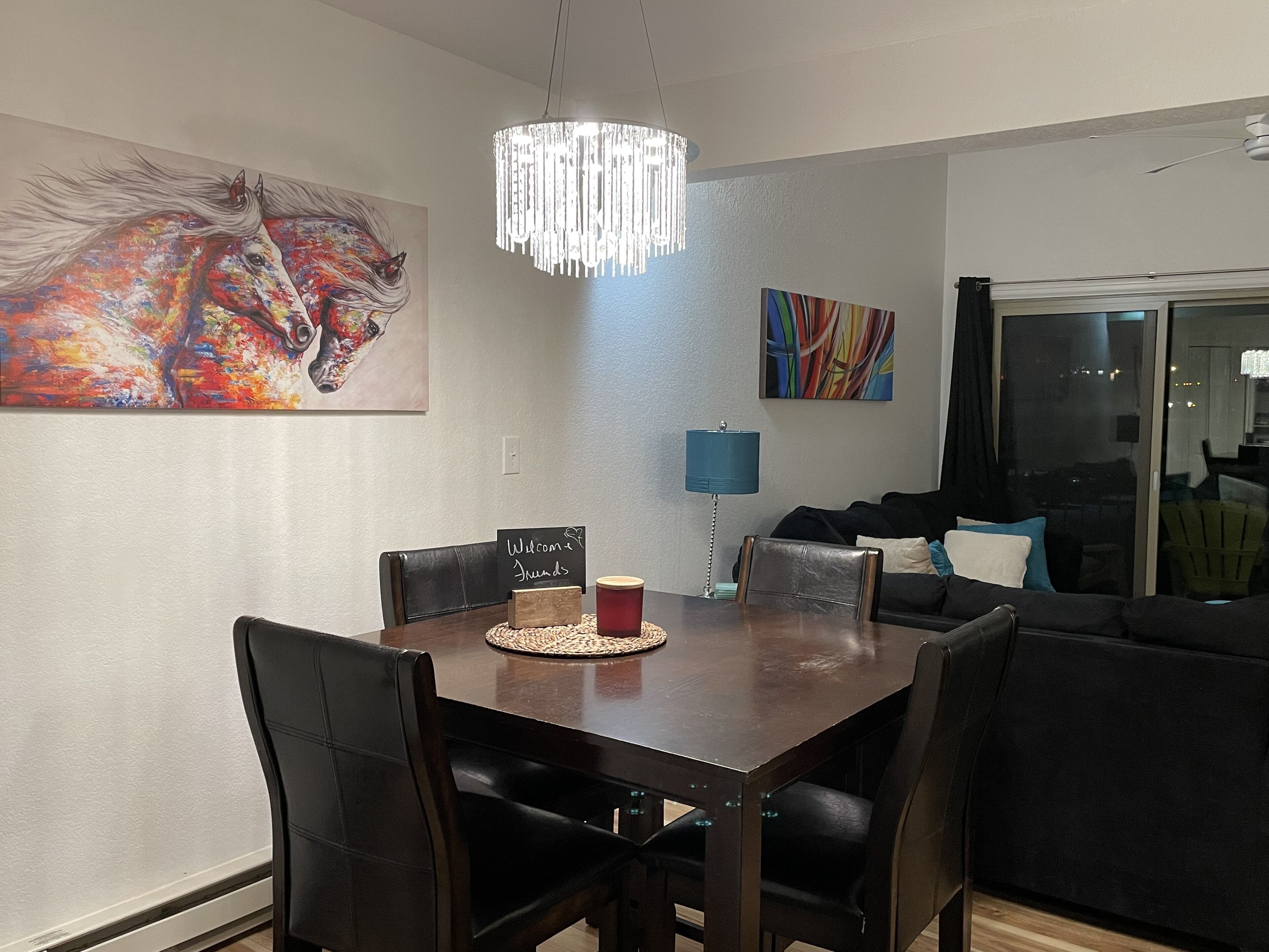 A dining area with a dark wooden table, black chairs, a chandelier, and two paintings on the walls.