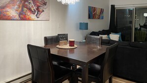 Un espace repas comprenant une table en bois, des chaises noires, un lustre et des œuvres d’art accrochées aux murs.