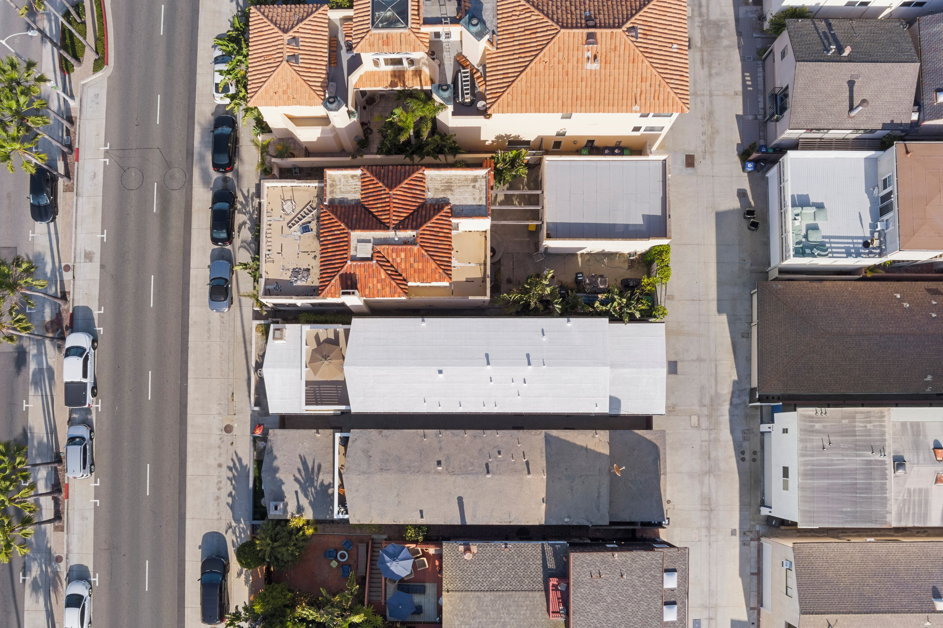 Luftaufnahme eines Gebäudes mit Dachterrasse, Parkplatz und angrenzenden Bauten.