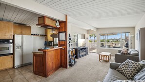 Een moderne keuken met houten kastjes, een inbouwkoelkast en een bar. Er is een woonkamer met een bank en uitzicht op de omgeving.