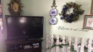A living room with a flat-screen TV on a stand, a white picket fence, and a welcome sign on the wall. - Private one bedroom, one bathroom, apartment with private entrance & hot tub (Branson)