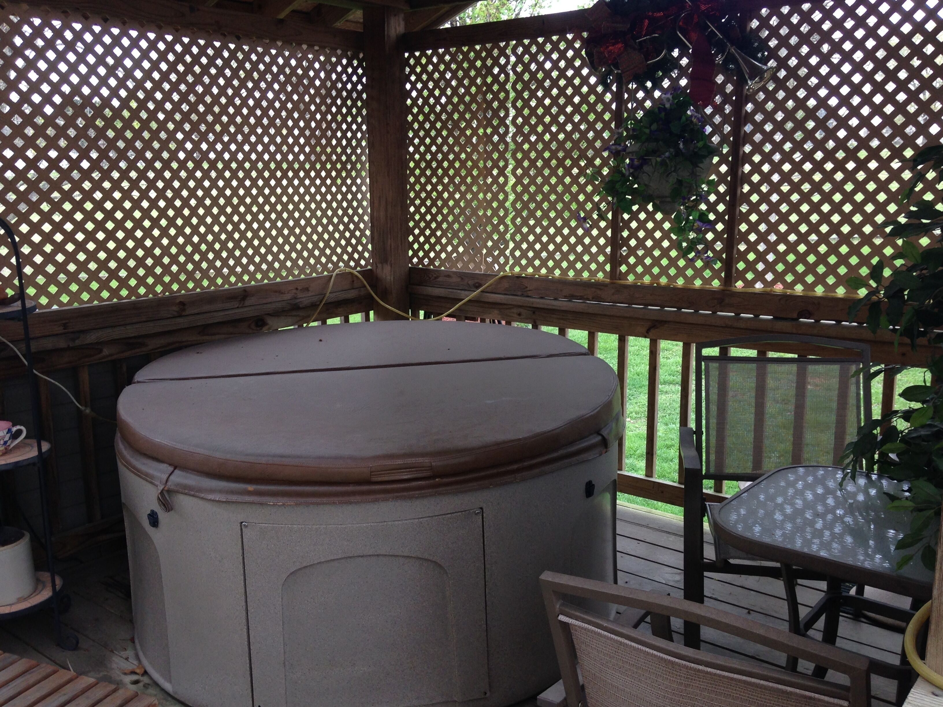 Un jacuzzi en un espacio exterior cubierto con terraza de madera, una mesa y sillas.