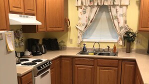 A kitchen with wooden cabinets, a stove, a sink, and a window with floral curtains. - Private one bedroom, one bathroom, apartment with private entrance & hot tub (Branson)
