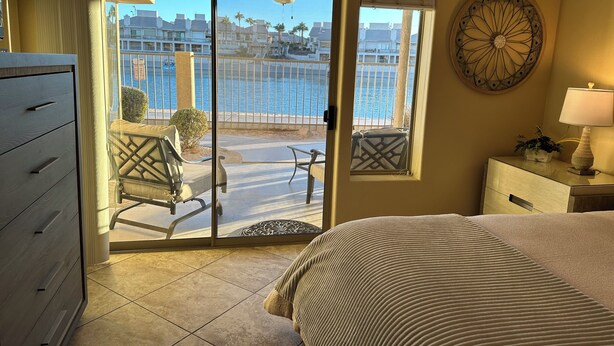 A hotel room with a bed, a dresser, a desk with a lamp, a view of the pool and buildings through a sliding glass door.