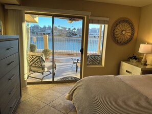 Une chambre d’hôtel avec un lit, une commode, un bureau avec une lampe, et une vue sur la piscine et les bâtiments, visible à travers une porte-fenêtre coulissante.