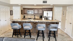 A kitchen with a central island, bar stools, and a refrigerator.