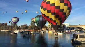 A river with multiple hot air balloons and boats.