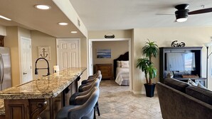 A modern kitchen with a granite countertop, bar stools, and a ceiling fan.