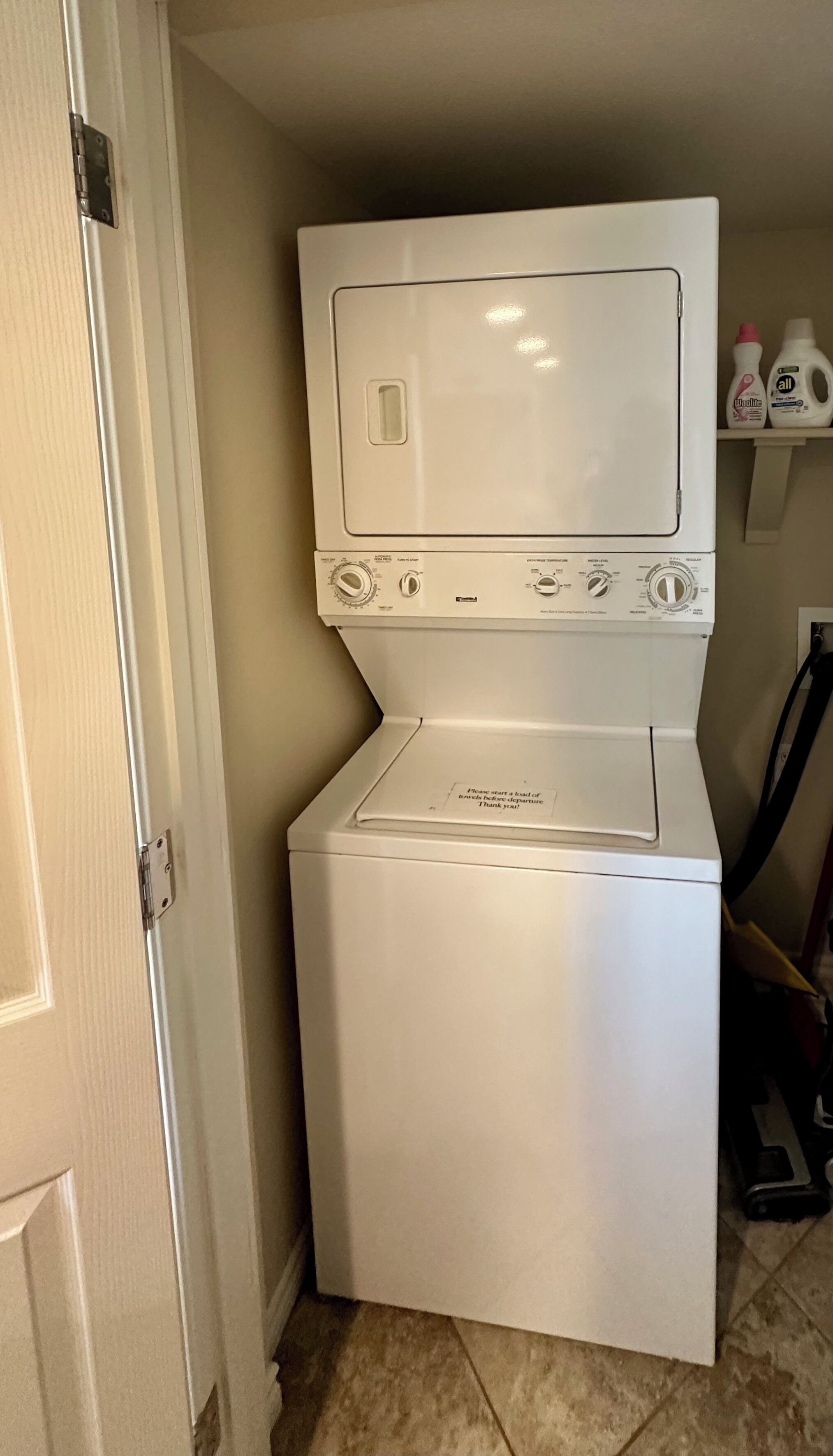 A compact washer and dryer unit with a control panel, located in a small laundry room with a tiled floor.