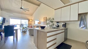 A modern kitchen with white cabinets, a central island, and a dining area with a sofa and chairs.