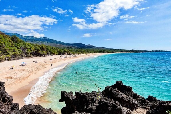 A beach with clear turquoise waters, a sandy shore, and rocky outcrops.