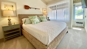 A bedroom with a large bed, a wooden headboard, two bedside tables with lamps, a wall-mounted guitar, and a window with blinds.
