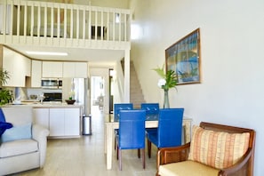 A spacious living area with a dining table, blue chairs, a sofa, and a kitchen in the background.