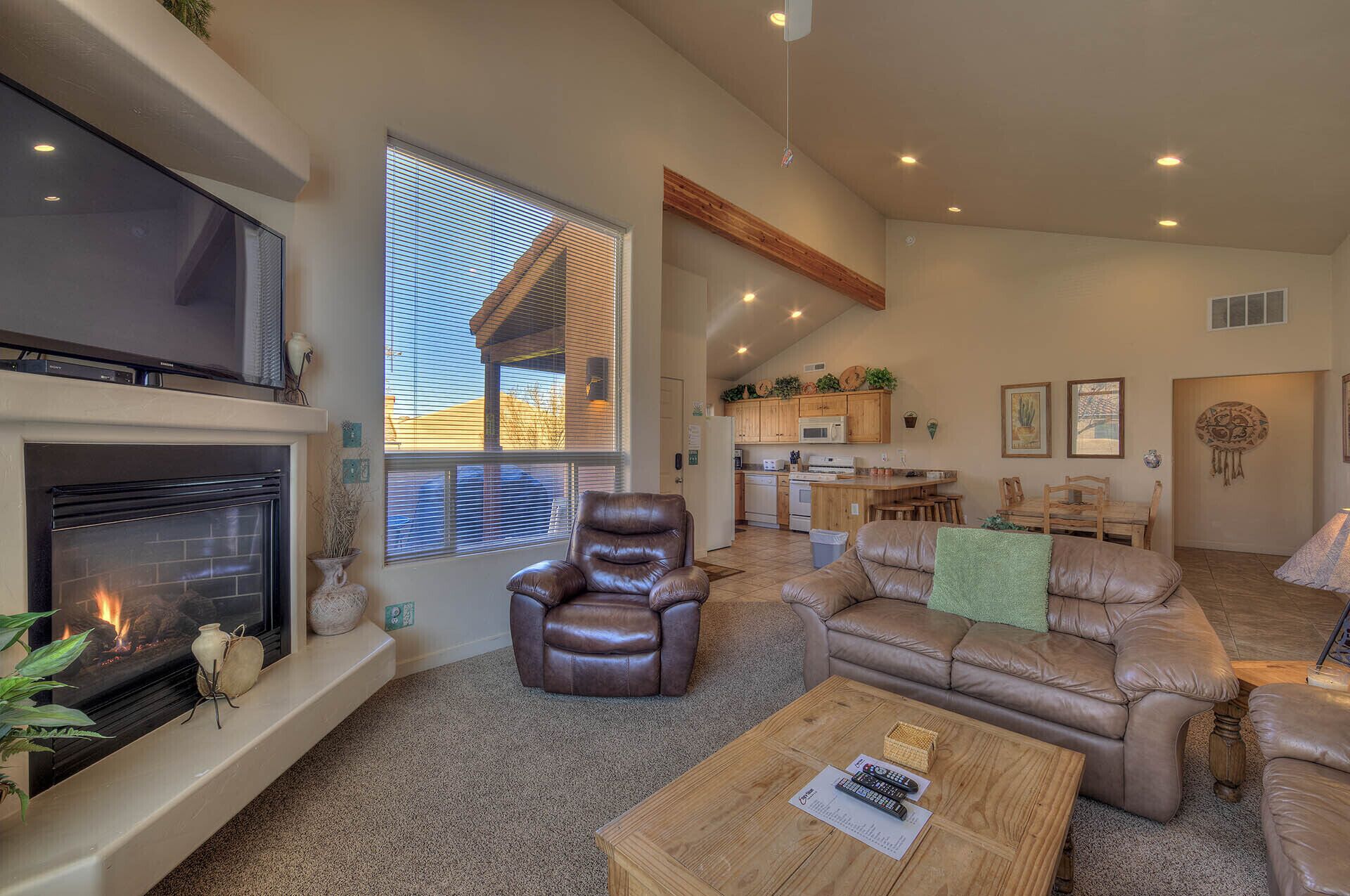 A spacious living room with a fireplace, leather sofas, a coffee table, and a kitchen in the background.