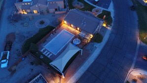 Eine Vogelperspektive zeigt eine Wohngegend mit einem Haus, das einen Swimmingpool, Sitzmöglichkeiten im Freien und eine gepflegte Rasenfläche besitzt.
