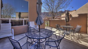 Eine Terrasse im Freien mit einem runden Metalltisch und Stühlen, einem Sonnenschirm und Blick auf ein Gebirge.