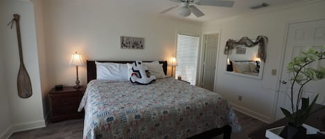 A bedroom with a bed, nightstands, a ceiling fan, a lamp, a door, and a plant.