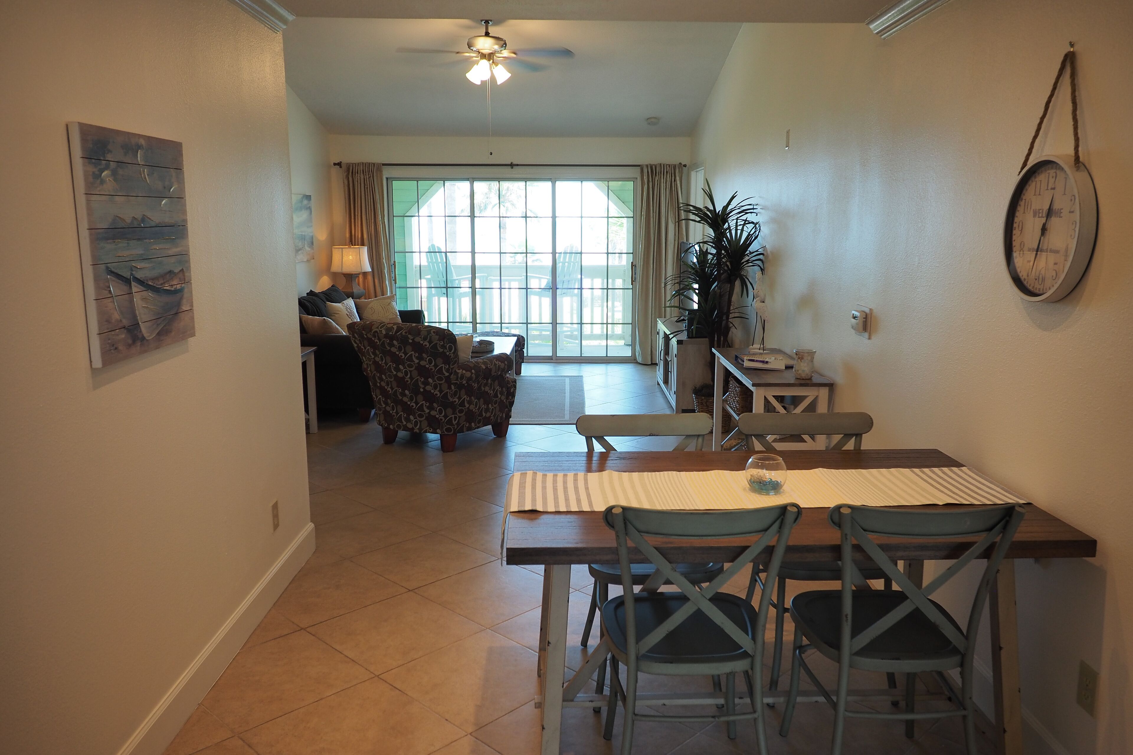 A dining area with a table and chairs, a ceiling fan, and a view to a living room with a sofa and a lamp.