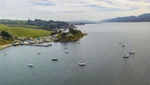 Uma vila costeira com barcos atracados em um cais, cercada por colinas e um mar calmo.