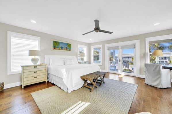A bedroom with a bed, a ceiling fan, a window with blinds, a painting, and a balcony view.