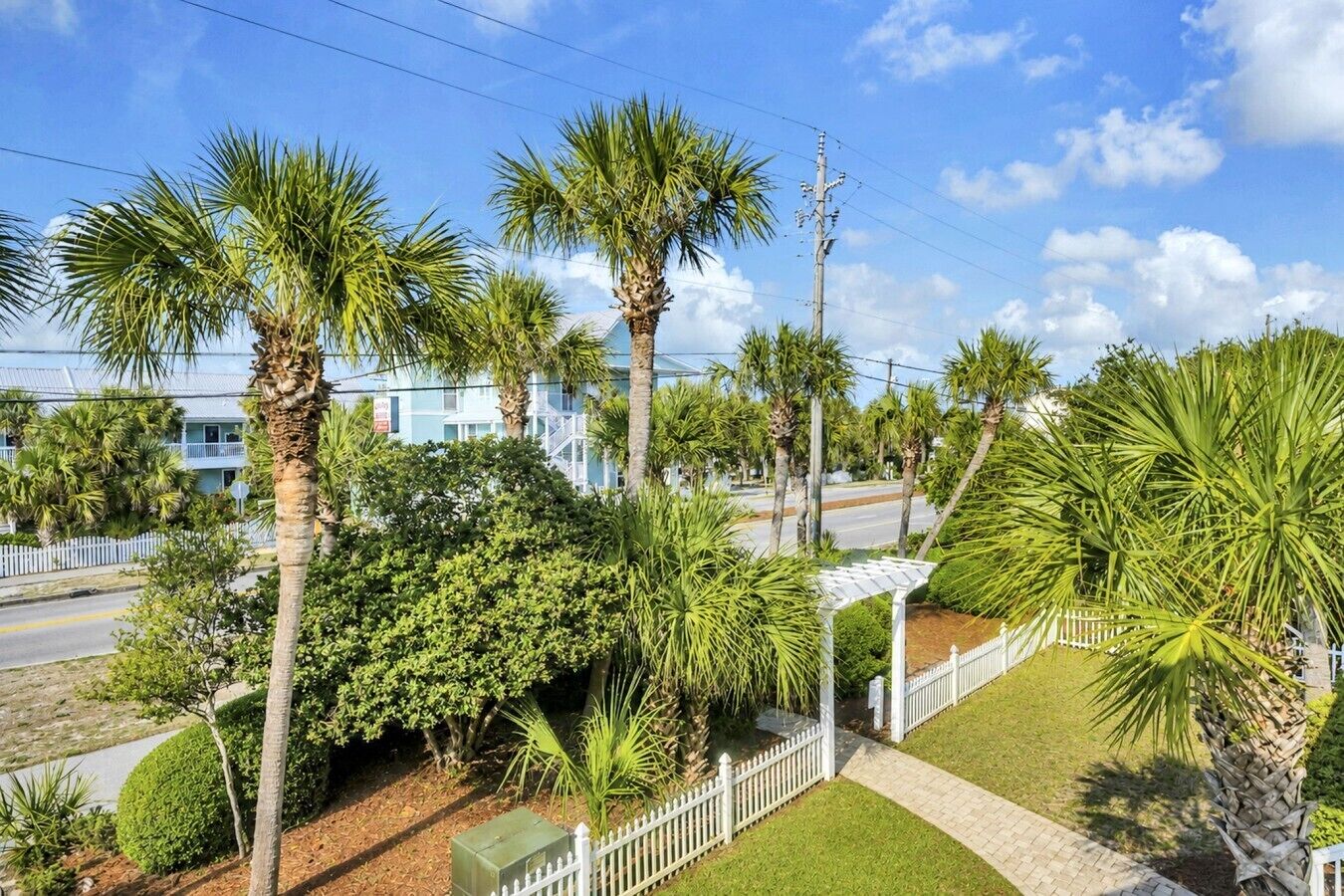 A residential area with palm trees, a white picket fence, and a road.