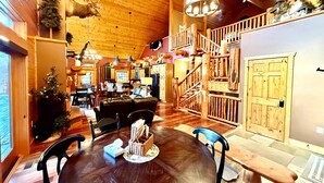 A rustic interior with a wooden ceiling, a round dining table, and a staircase with a wooden railing.