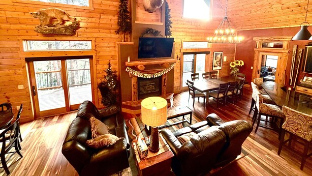 A log cabin interior with a fireplace, a mounted deer head, a television, and a dining area.
