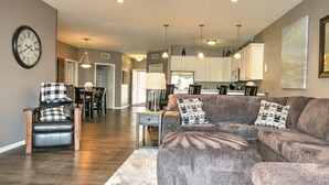 A modern living room with a gray sofa, a dining area with a table and chairs, and a kitchen in the background.