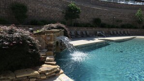 A swimming pool with a stone waterfall feature, lounge chairs, and a stone wall.
