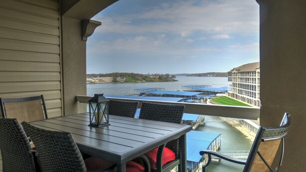 A balcony with a table and chairs, overlooking a body of water with docks and buildings.