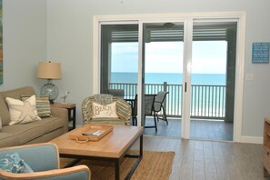 A living room with a sofa, a coffee table, and a chair. There is a view of the ocean through a sliding glass door. - "Turtle Haven" Direct Ocean Front 5th floor Condo on Cinnamon Beach. Unit 553 (Palm Coast)
