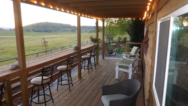 A covered outdoor deck with wooden flooring, bar stools, and lounge chairs.