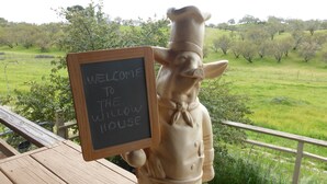 A wooden sign with "WELCOME TO THE WILLOW HOUSE" written on it, held by a statue of a chef.