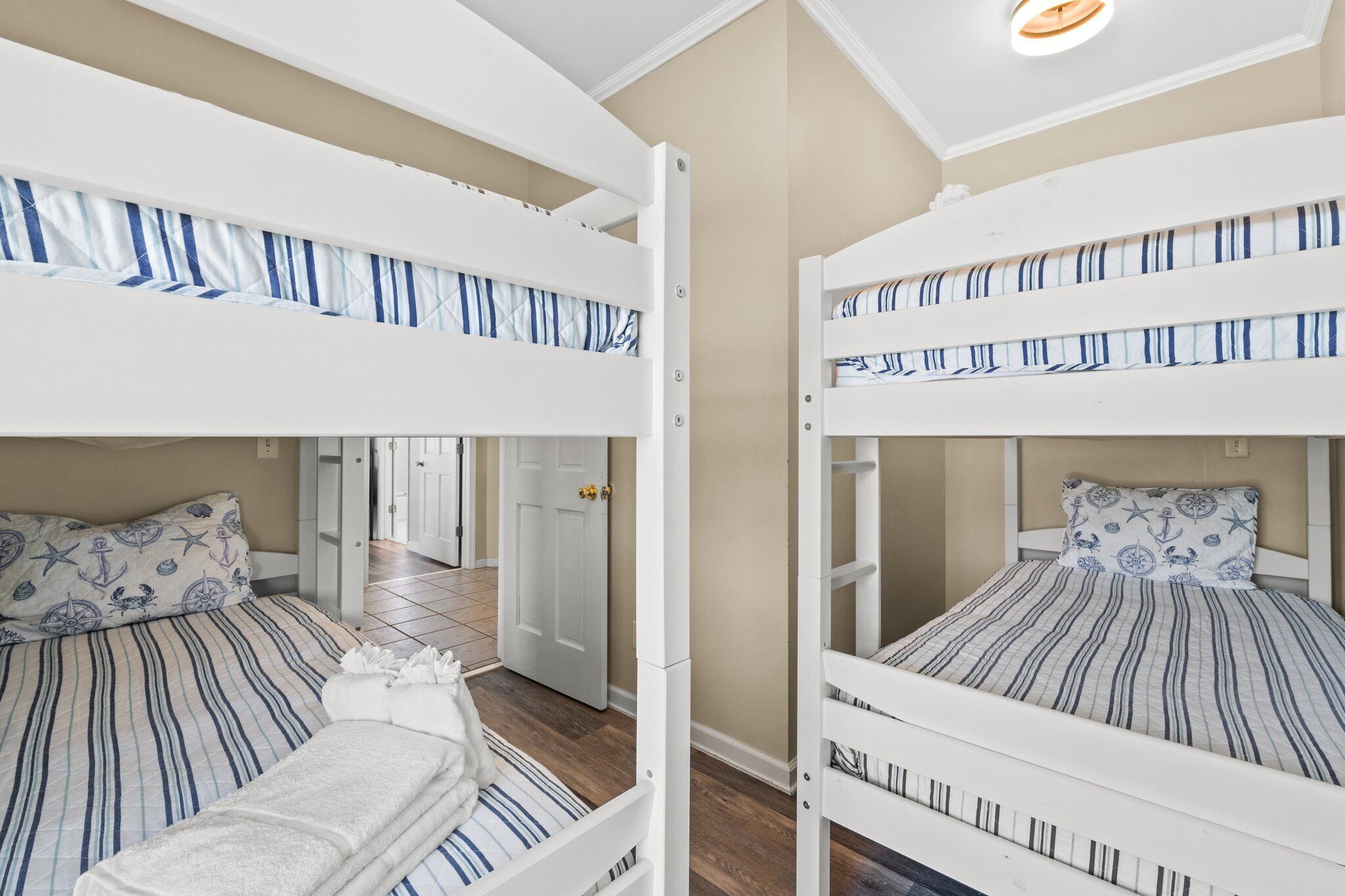 A room with two bunk beds, each with striped bedding and a pillow with a nautical theme.