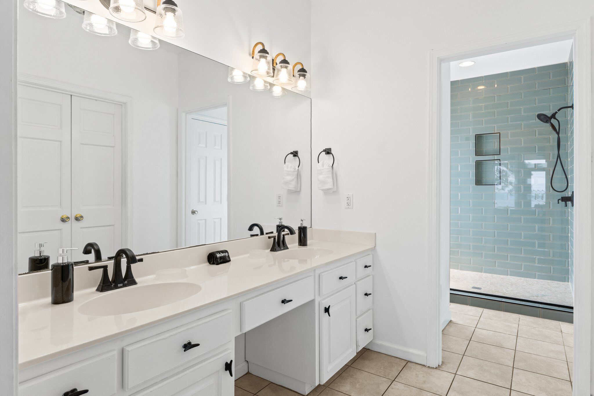A modern bathroom with two sinks, a large mirror, and a shower area with blue tiles.