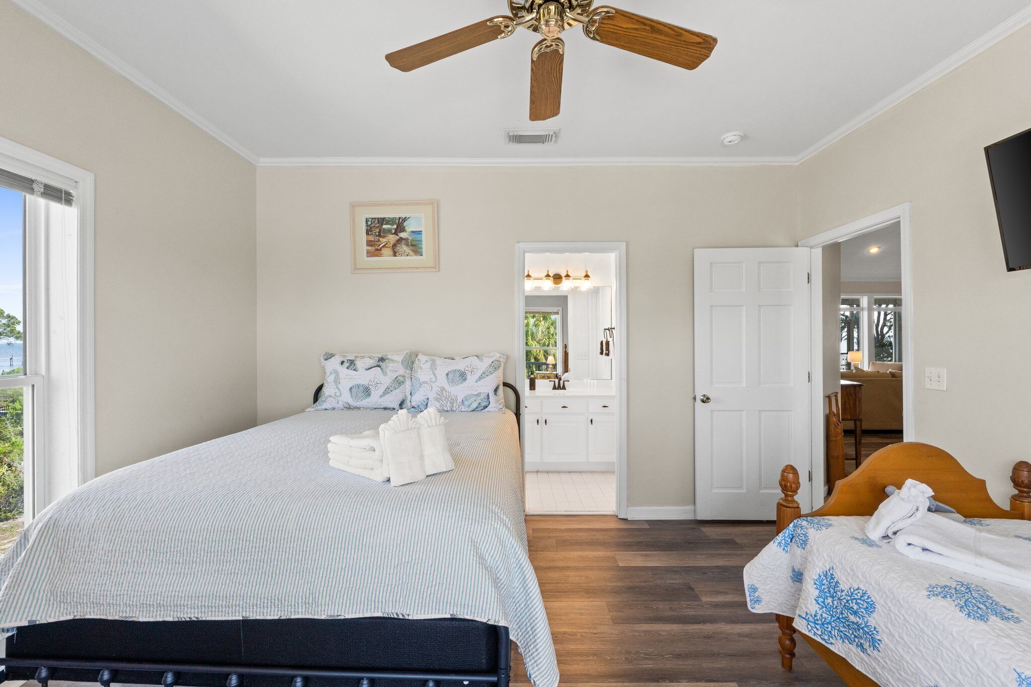 Une chambre à coucher comprenant un lit, un plus petit lit, un ventilateur de plafond, une salle de bain avec un lavabo et une porte donnant sur une autre pièce.