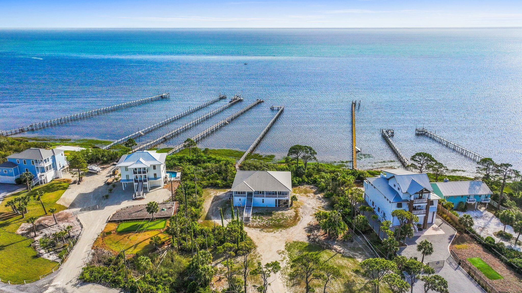 A coastal property with multiple houses connected by piers to the water, featuring a sandy beach and lush greenery.