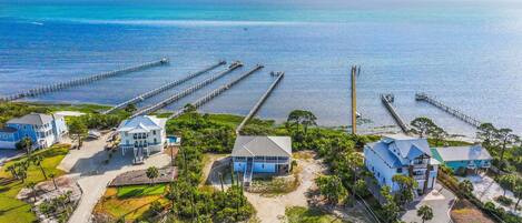 A coastal property with multiple houses connected by piers to the water, featuring a sandy beach and lush greenery.