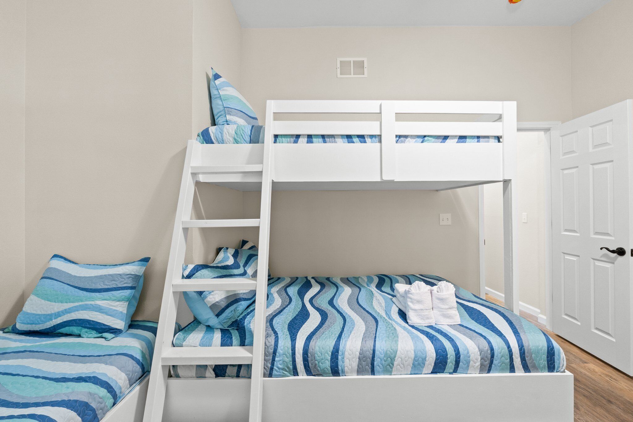 Uma cama beliche com escada, uma cama de solteiro com colcha listrada e um guarda-roupa branco.