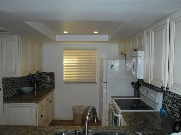 A kitchen with white cabinets, a granite countertop, a built-in oven, and a window with blinds. - Newly Remodeled, ocean view condo on top floor at Spanish Main (Cocoa Beach)