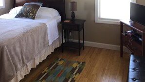 A bedroom with a bed, a nightstand, a lamp, a television, a window, and a painting on the wall. - Relaxing Hampton Beach Vacation Home (Hampton)