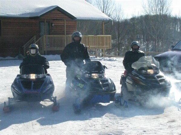 Three snowmobiles parked in a snowy area with a wooden building in the background.