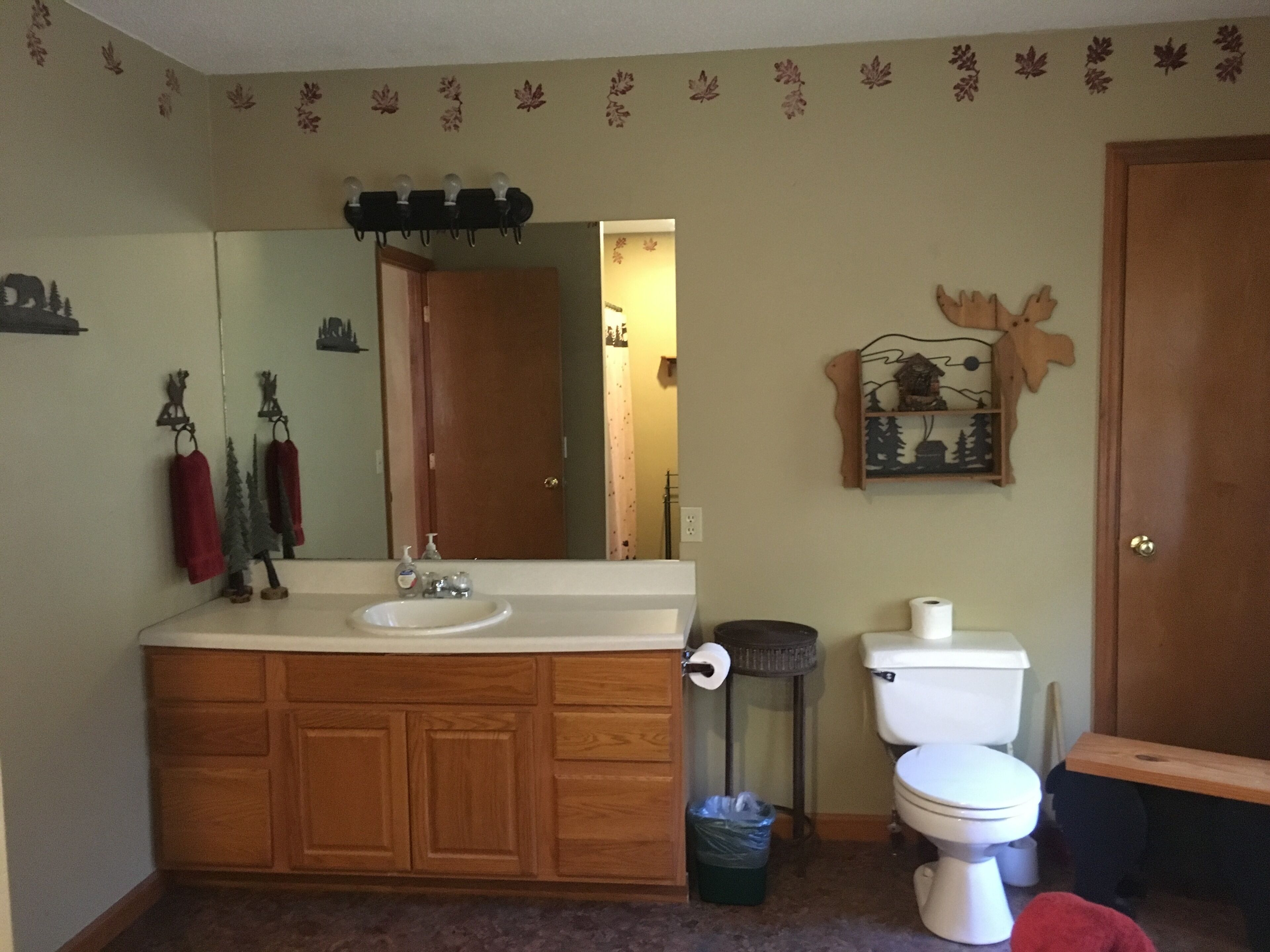 A bathroom with a wooden vanity, sink, mirror, toilet, and a trash can.