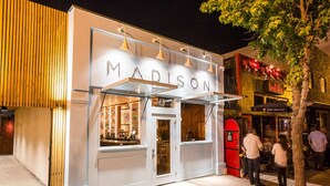 A storefront with the name 'MADISON' illuminated at night, featuring a modern design with a glass facade and a wooden panel on the left.