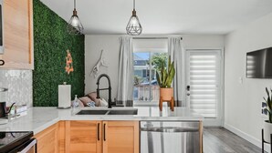 A modern kitchen with a green wall, wooden cabinets, a stainless steel refrigerator, and pendant lights.