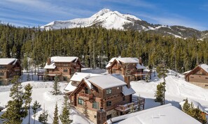 Un complexe hôtelier composé de plusieurs chalets en bois, dont les toits sont recouverts de neige, avec une montagne enneigée en toile de fond.