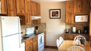 Una cocina con armarios de madera, un refrigerador blanco, una estufa y una mesa de comedor con sillas.